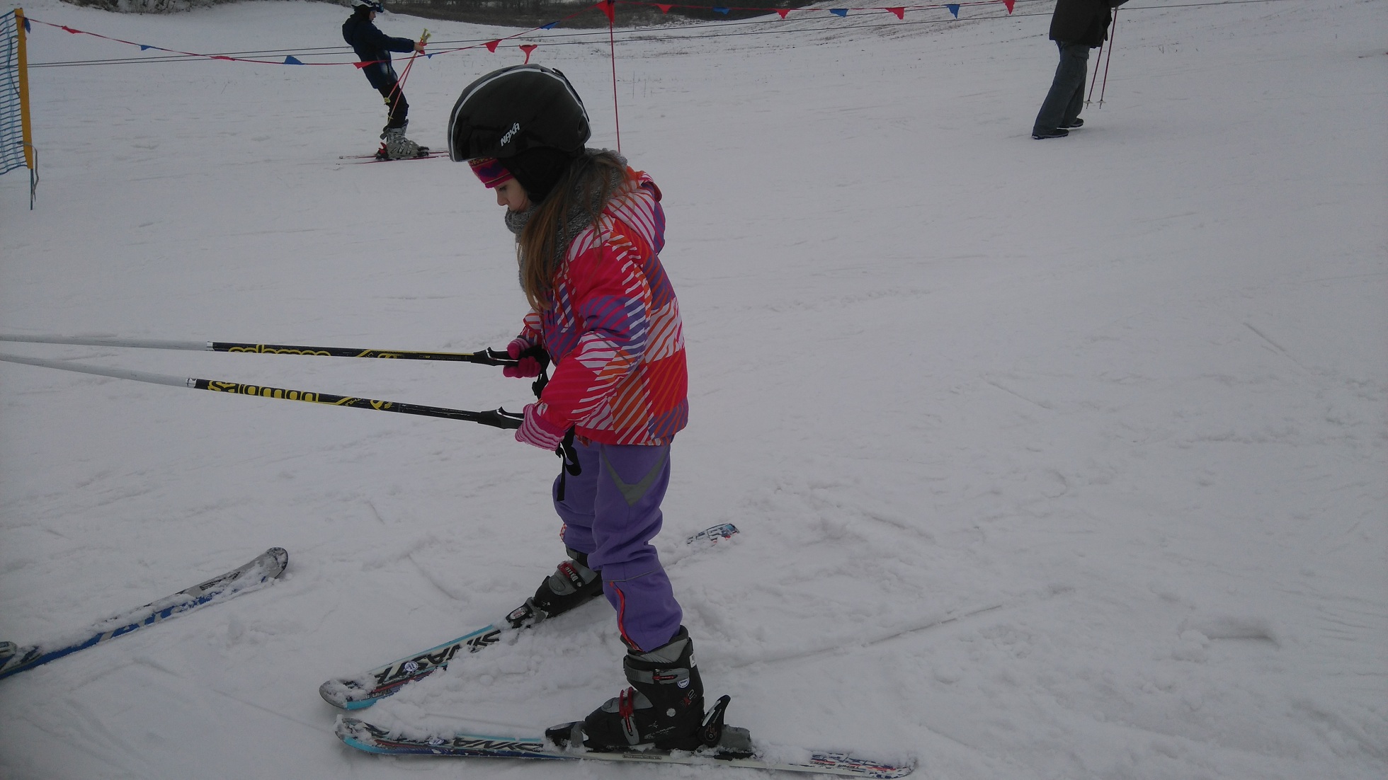 dziewczynka w stroju narciarskim zjeżdża z górki trzymając za kijki